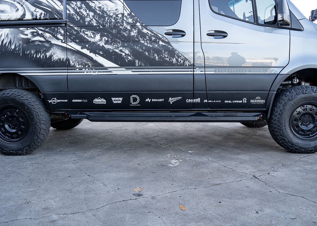 Direct side profile of ROAMBUILT Flat Side Step in black textured aluminum, mounted on a Mercedes Sprinter, showing full length and clearance.