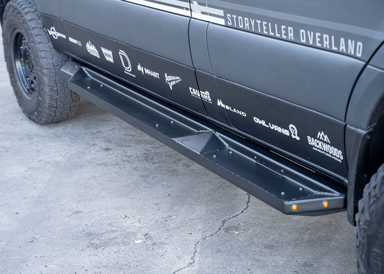 Front-to-back passenger side view of ROAMBUILT Flat Side Step on Mercedes Sprinter, showing black aluminum finish and integrated and small lights.