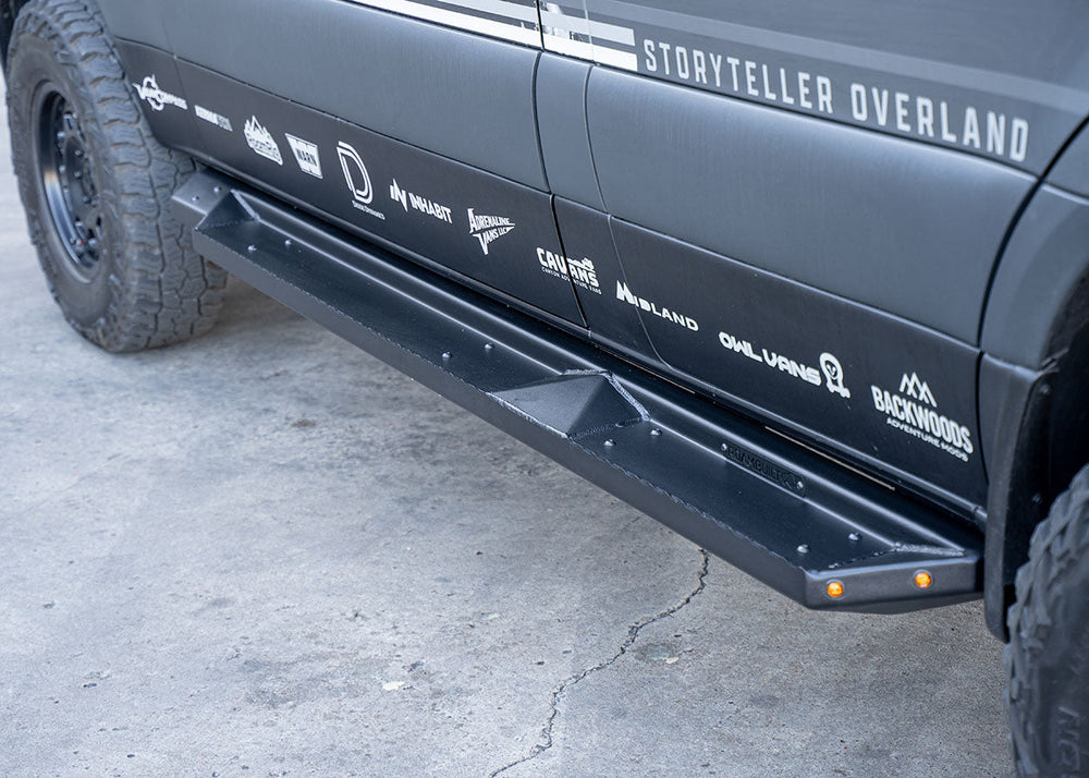 Front-to-back passenger side view of ROAMBUILT Flat Side Step on Mercedes Sprinter, showing black aluminum finish and integrated and small lights.
