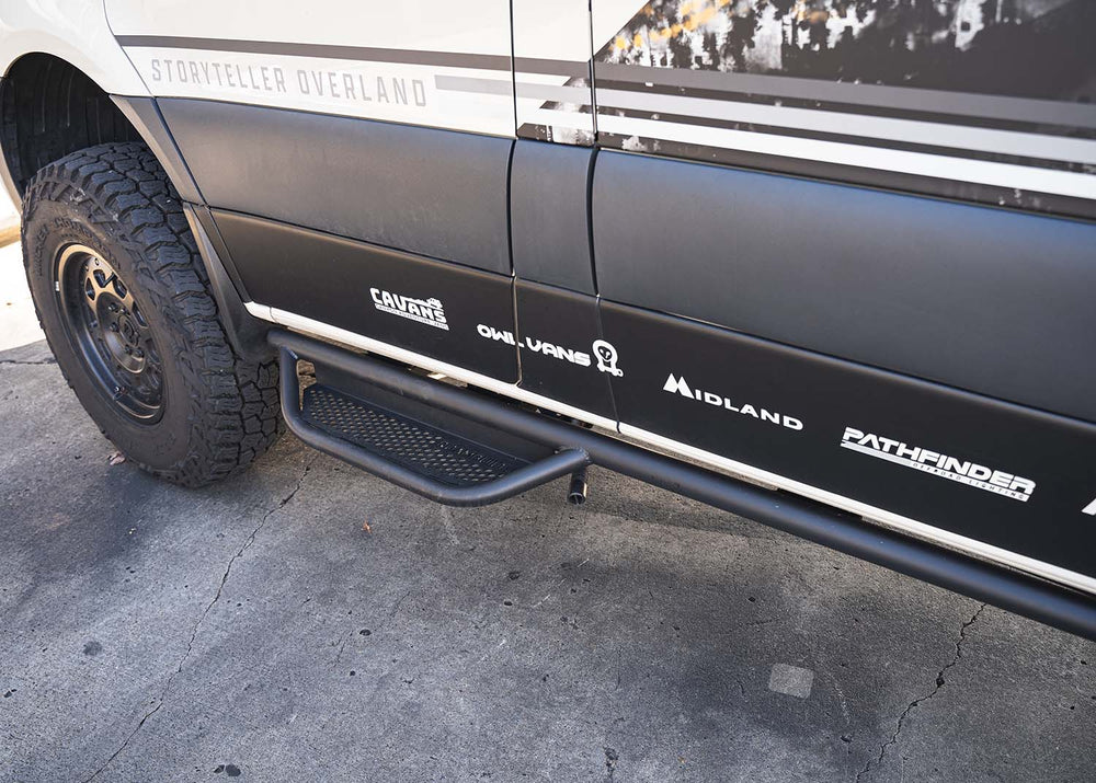 Driver side view looking from the rear toward the front, showcasing the full ROAMBUILT Mercedes Sprinter Side Step mounted under the van with visible perforated aluminum decking 