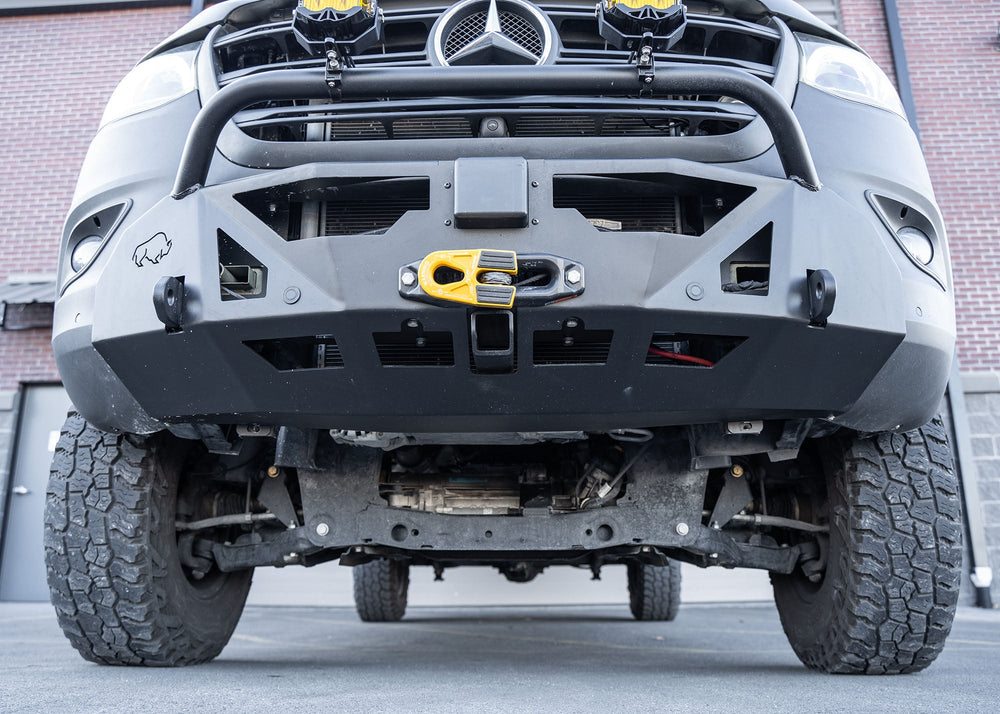 Close-up of the lower section of a Mercedes-Benz Sprinter's ROAMBUILT LoPro Front Bumper, highlighting the integrated steel 2-inch receiver hitch and 1-inch thick shackle mounts, all encased within a lightweight 5052 aluminum outer shell.