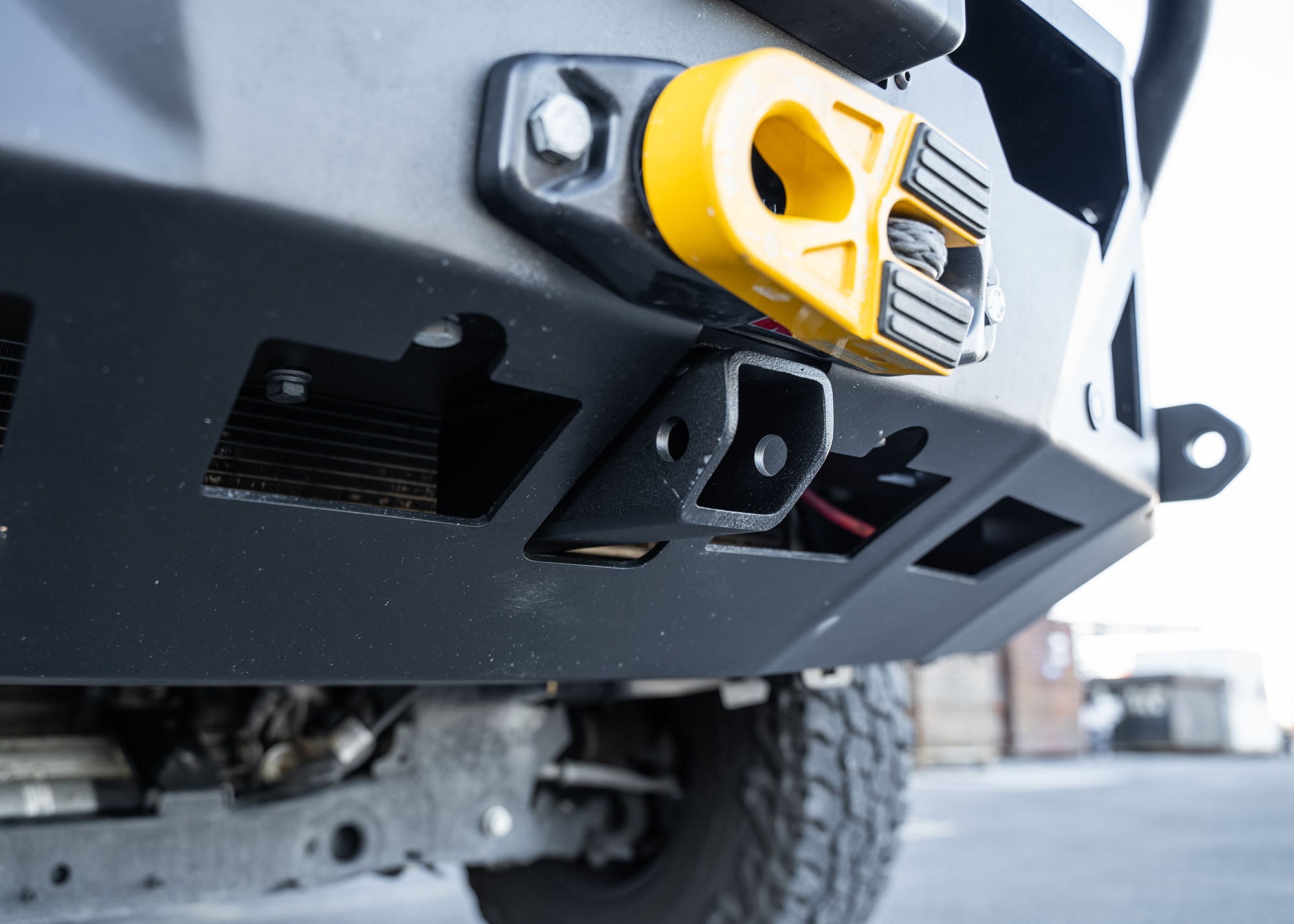 Close-up of the underside of a Mercedes-Benz Sprinter van's ROAMBUILT LoPro Front Bumper, showcasing the integrated 2-inch receiver hitch and hawse fairlead, all encased within a lightweight 5052 aluminum shell.